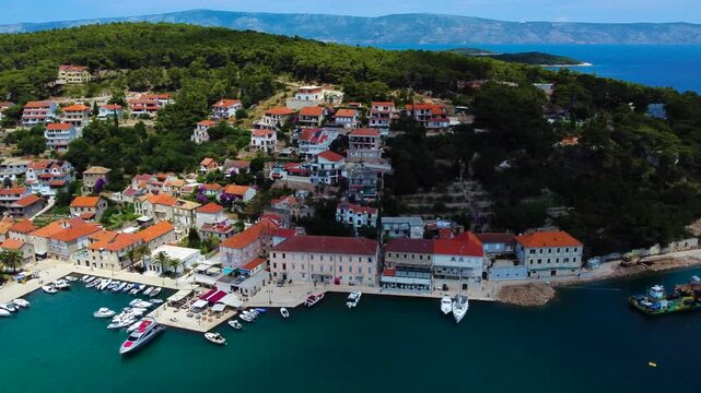 Aerial view of Jelsa harbor with boats docked along the waterfront, surrounded by red-tiled Mediterranean houses and lush green hills in Jelsa, Split-Dalmatia County, Croatia.