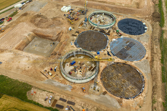 Aerial view of a construction site with large circular concrete foundations, heavy machinery, and a yellow tower crane in Lithuania.