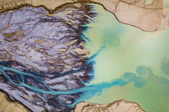 Aerial view of the river delta near Prutz, featuring intricate sediment patterns and vibrant turquoise glacial water flowing into a larger body of water in Prutz, Tyrol, Austria.