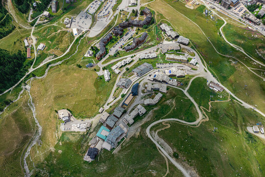 Aerial view of the Breuil-Cervinia ski resort area featuring alpine buildings, winding roads, and green mountain slopes in Breuil-Cervinia, Aosta Valley, Italy.