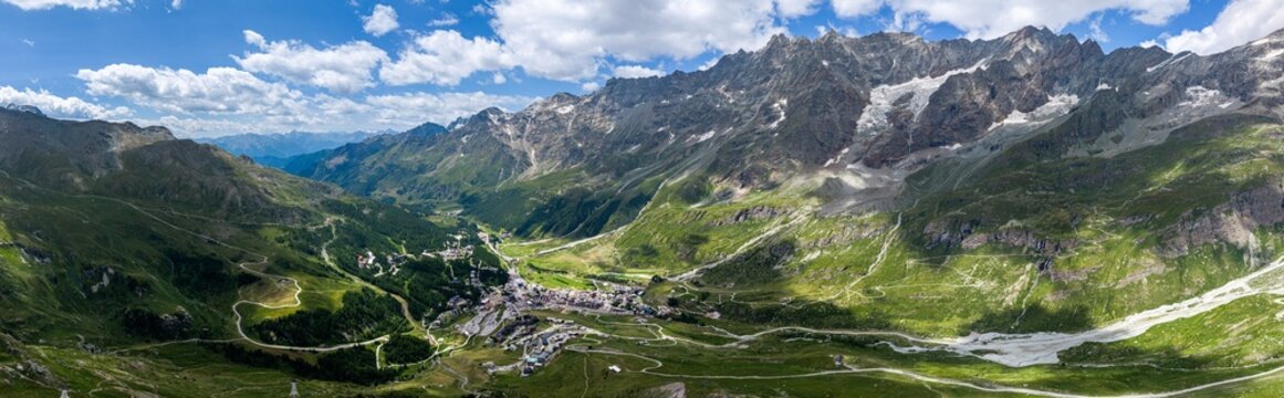 Aerial view of the alpine village of Breuil-Cervinia nestled in a lush green valley surrounded by rocky mountain peaks and winding roads in Breuil-Cervinia, Aosta Valley, Italy.