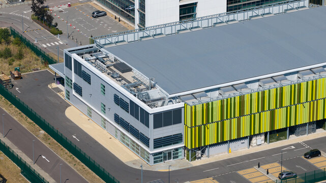 Aerial view of the Kao Data facility with green and yellow facade panels, a flat grey roof, and surrounding parking areas in Harlow, England, United Kingdom.