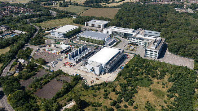Aerial view of the Kao Data campus featuring modern data center buildings surrounded by lush woodland and access roads in Harlow, England, United Kingdom.
