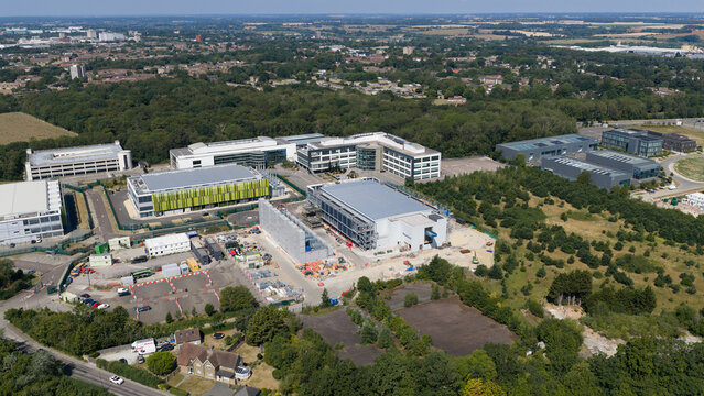 Aerial view of the Kao Data campus featuring modern office buildings and a construction site surrounded by lush greenery in Harlow, England, United Kingdom.