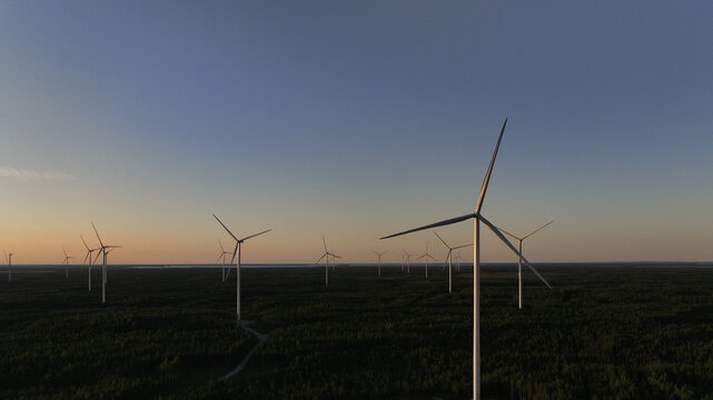 Aerial view of Metsalamminkangas Tuulipuisto wind farm with large turbines rising above the dense forest during golden hour in Siikalatva, Pohjois-Pohjanmaa, Finland.