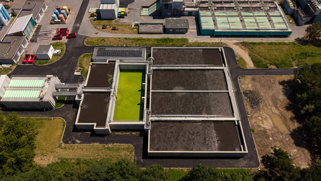 Aerial view of a wastewater treatment plant featuring large aeration tanks with green and dark water, industrial infrastructure, and surrounding greenery in Milan, Lombardy, Italy.