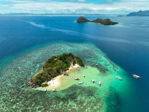 Aerial view of CYC Beach with turquoise waters, coral reefs, and traditional outrigger boats surrounding the small island in Coron, Mimaropa, Philippines.