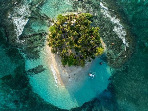 Aerial view of Guyam Island with dense palm trees, white sand beach, and turquoise water surrounded by coral reefs in General Luna, Caraga, Philippines.