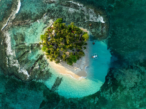 Aerial view of Guyam Island with lush palm trees, white sand beach, and turquoise waters surrounded by coral reefs in General Luna, Caraga, Philippines.