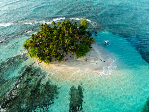 Aerial view of Guyam Island featuring lush palm trees, a white sand beach, and clear turquoise water with a small boat anchored nearby in General Luna, Caraga, Philippines.