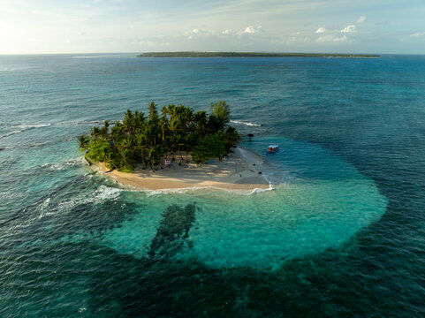 Aerial view of Guyam Island with its lush palm trees, white sandy beach, and turquoise waters surrounded by the deep blue sea in General Luna, Caraga, Philippines.