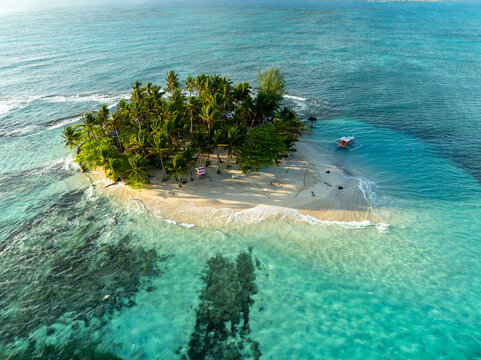 Aerial view of Guyam Island with lush palm trees, white sand beach, and turquoise waters in General Luna, Caraga, Philippines.