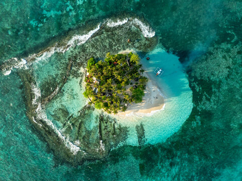 Aerial view of Guyam Island featuring lush palm trees and a white sand beach surrounded by turquoise water and coral reefs in General Luna, Caraga, Philippines.
