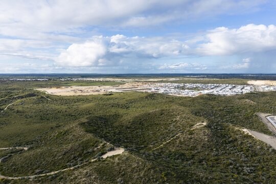 Aerial view of a residential development surrounded by native bushland and rolling hills under a cloudy sky in Perth, Western Australia, Australia.
