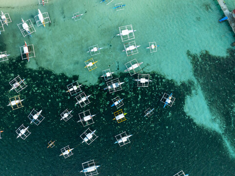 Aerial view of traditional outrigger boats floating in the turquoise waters surrounding Naked Island, with coral reefs visible beneath the surface in Siargao, Philippines.