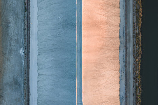 Aerial view of giant white salt mounds in the Camargue salt marshes, featuring geometric patterns created by warm evening light and cool blue shadows, France.
