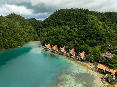Aerial view of Bucas Grande featuring a row of stilt bungalows nestled along a turquoise lagoon surrounded by lush tropical hills in Siargao, Philippines.