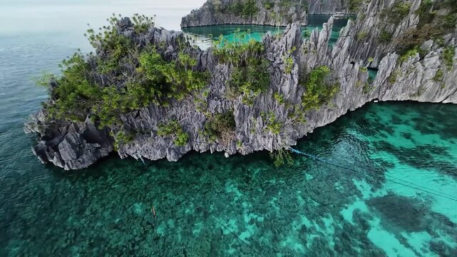 FPV aerial view of Pass Island featuring limestone cliffs, turquoise coral reefs, and a floating structure in the clear water of Culion, Mimaropa, Philippines.