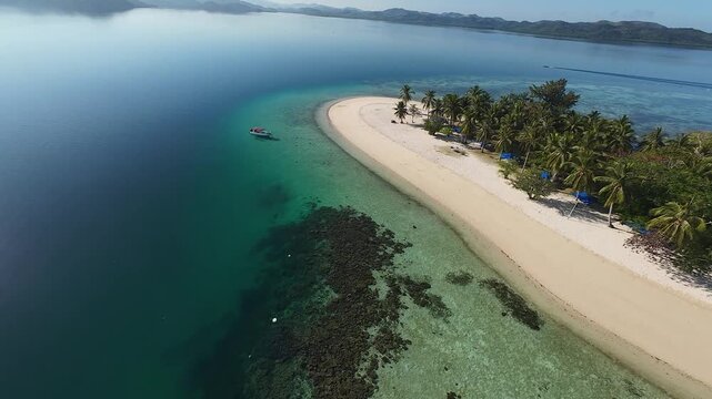 FPV aerial view of Pass Island with its white sand beach, palm trees, and clear turquoise water surrounded by coral reefs in Culion, Mimaropa, Philippines.
