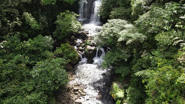 Aerial view of a cascading waterfall surrounded by dense tropical rainforest and lush green vegetation in Banyumas Regency, Central Java, Indonesia.