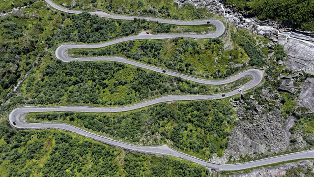Aerial view of a winding mountain road with sharp hairpin turns surrounded by lush green vegetation and rocky terrain in Nordland, Norway.