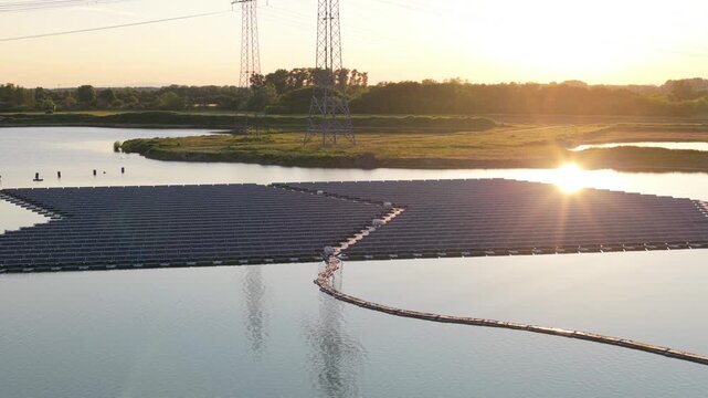 Aerial view of the floating solar park by Rohr on a lake during golden hour with power lines in the background in Bensheim, Hessen, Germany.