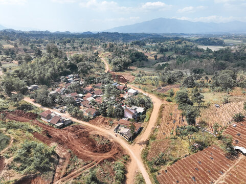Aerial view of a small rural village surrounded by terraced agricultural fields, dirt roads, and lush green hills in Garut, West Java, Indonesia.