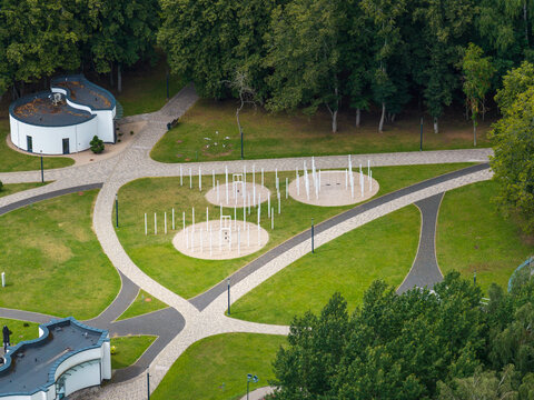 Aerial view of the sculpture park in Elektrenai featuring white vertical pillars in circular formations on green lawns with paved pathways and trees in Elektrenai, Vilnius County, Lithuania.