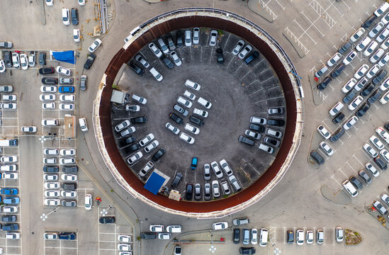 Aerial view of a circular car lot filled with numerous parked vehicles, surrounded by paved parking areas and urban infrastructure in Ramat Hasharon, Tel Aviv District, Israel.
