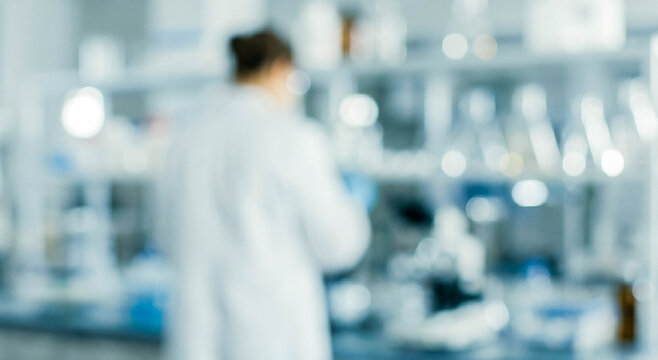 A blurred background of a laboratory setting with a scientist in a white coat working. Equipment and glassware are visible on shelves behind them.