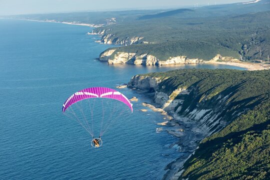Aerial view of a paramotor flying over the scenic Cilingoz coastline with steep cliffs, lush forests, and the deep blue Black Sea in Catalca, Istanbul, Turkey.