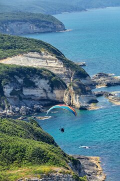 Aerial view of a paraglider soaring over the rugged cliffs and turquoise waters of Yalikoy in Catalca, Istanbul, Turkey.