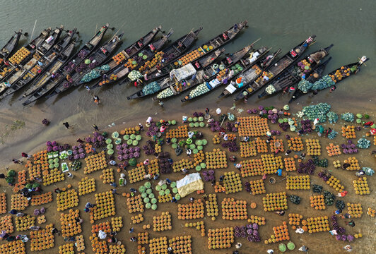 Aerial view of the floating market in Sylhet with wooden boats laden with fresh vegetables arranged in rows along the riverbank in Sylhet, Sylhet Division, Bangladesh.