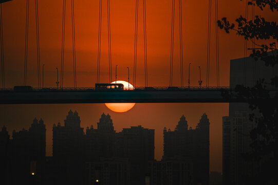 View of the Lupu Bridge entrance with traffic silhouetted against a vibrant orange sunset over the Shanghai skyline in Shanghai, Shanghai, China.