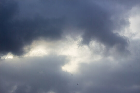 Dramatic storm clouds with bright light breakthrough, dark overcast sky texture, moody atmospheric weather background