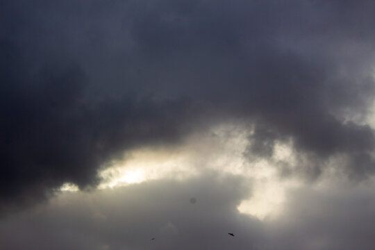 Dramatic storm clouds with bright sunlight breaking through, dark overcast sky, moody weather background