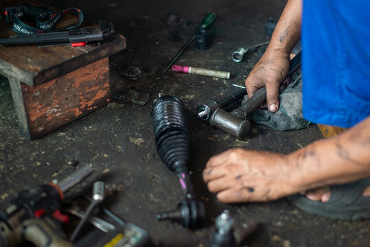Auto repair technician working on vehicle tie rod and steering components with hand tools, authentic photo, not AI.