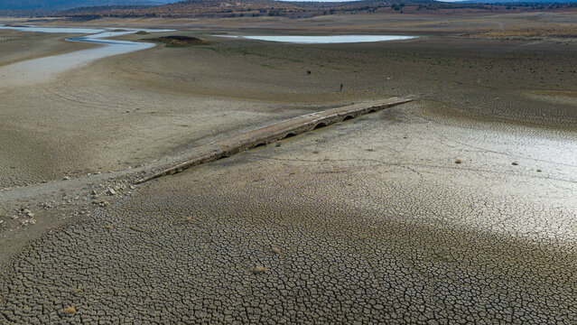 Aerial view of the historic stone bridge exposed in the dried-up bed of Apa Dam, showing cracked earth and arid landscape in Cumra, Konya, Turkiye.