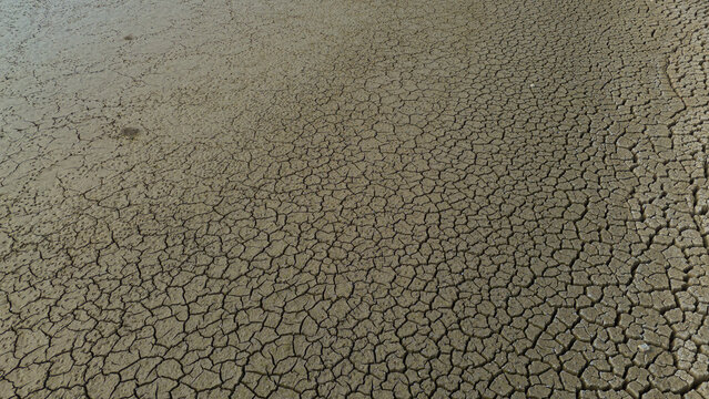 Aerial view of the cracked, parched earth at the dried-up bed of Apa Dam, showing intricate patterns of dry mud and soil in Cumra, Konya, Turkiye.