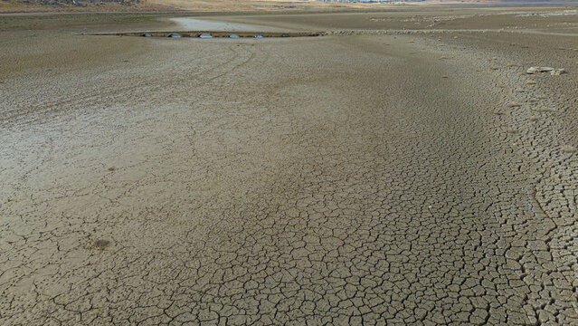 Aerial view of the cracked and arid bed of the Apa Dam reservoir, showing the effects of severe drought with an old stone bridge visible in the distance, Cumra, Konya, Turkiye.