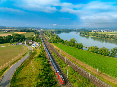 Aerial view of the night train from Hamburg to Vienna traveling along the Danube river through rural landscapes under a bright blue sky in Sarling, Lower Austria, Austria.