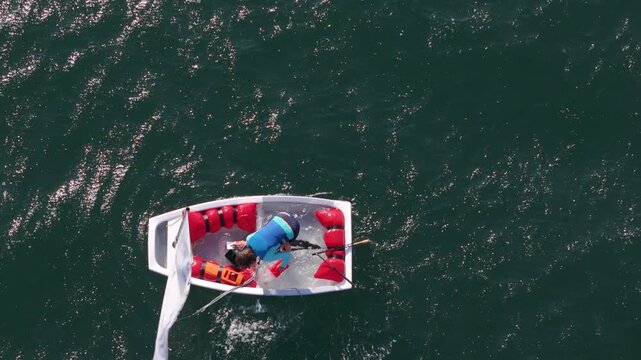 Aerial view of a person in a small capsized sailing boat with red safety equipment in the water near Cascais, Lisbon, Portugal.