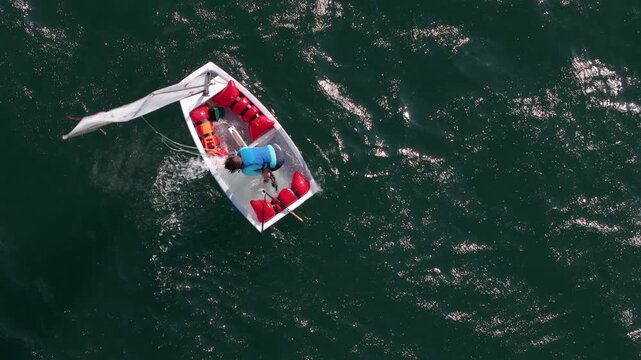 Aerial view of a person in a life vest struggling with a capsized small sailboat in the open water near Cascais, Lisbon, Portugal.