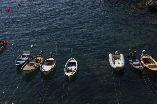 View of small wooden boats and a rubber dinghy moored in the clear blue waters of the harbor in Riomaggiore, Liguria, Italy.