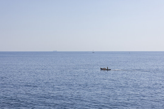 View of a small wooden boat with people sailing on the calm blue sea off the coast of Riomaggiore, Liguria, Italy.