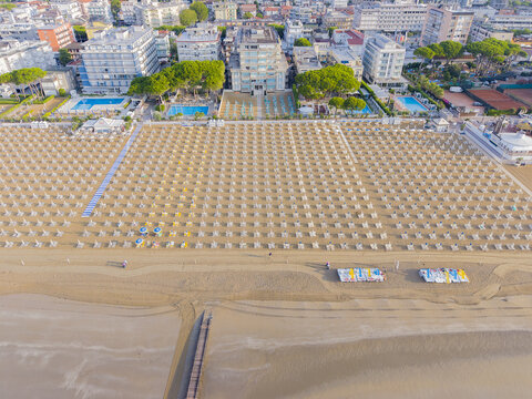 Aerial view of the sandy beach featuring dense rows of parasols and sun loungers, hotels, and swimming pools along the coastline in Lido di Jesolo, Veneto, Italy.