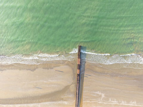 Aerial view of a wooden pier extending into the turquoise sea from the sandy beach of Lido di Jesolo, Veneto, Italy.