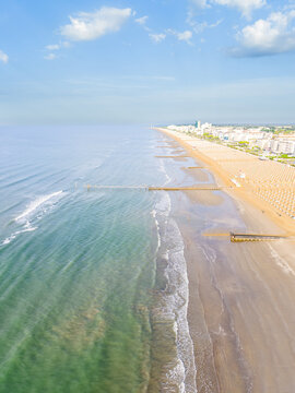 Aerial view of Lido di Jesolo beach with rows of umbrellas along the sandy coastline, calm turquoise sea, and clear blue sky in Lido di Jesolo, Veneto, Italy.