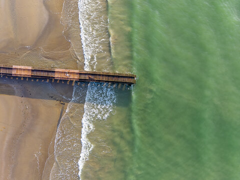 Aerial view of a wooden pier extending into the calm green sea at the sandy beach of Lido di Jesolo, Veneto, Italy.