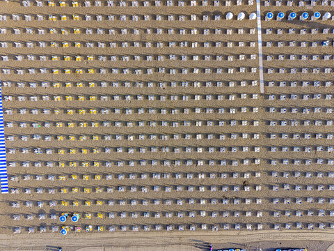 Aerial view of rows of beach umbrellas and sun loungers arranged in a grid pattern on the sandy beach of Lido di Jesolo, Veneto, Italy.